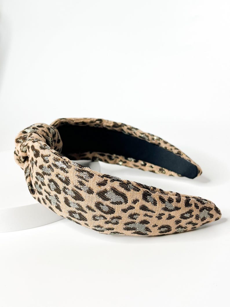 May include: A brown and black leopard print headband with a knotted detail. The headband is made of a soft, stretchy fabric.