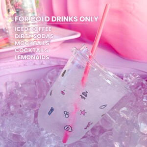 Op de afbeelding: Een doorzichtige plastic beker met deksel en roze rietje, gevuld met ijs en vloeistof. De beker heeft kleine geprinte iconen waaronder kersen, een bikini, een zeester en een wolkje met de letter b. Tekst: FOR COLD DRINKS ONLY.