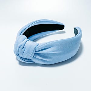 Puede incluir: Una diadema azul claro anudada. La diadema presenta un detalle de nudo cubierto de tela en el centro superior y un forro interior negro. La diadema es de color liso y est&aacute; dise&ntilde;ada para usarse en la cabeza.