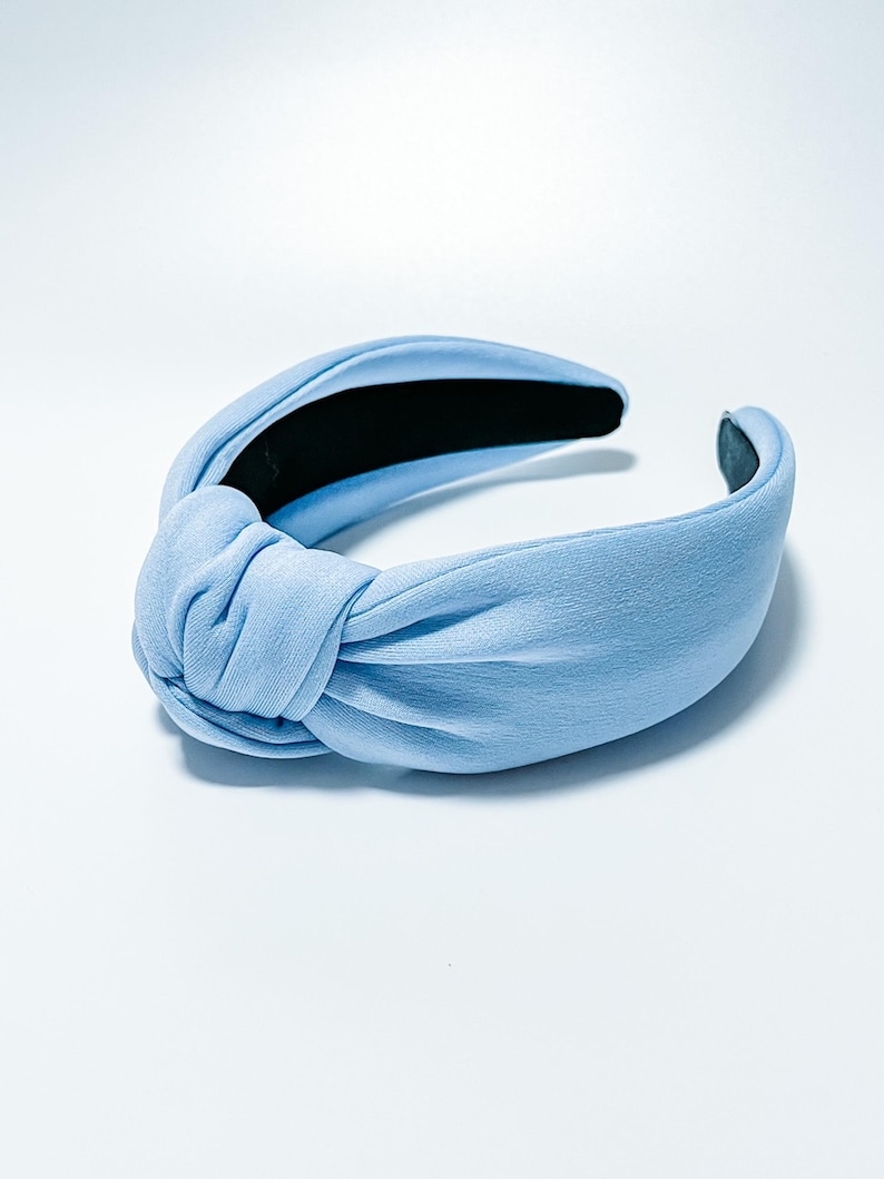 Puede incluir: Una diadema azul claro anudada. La diadema presenta un detalle de nudo cubierto de tela en el centro superior y un forro interior negro. La diadema es de color liso y est&aacute; dise&ntilde;ada para usarse en la cabeza.