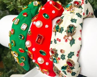 May include: Three Christmas-themed headbands with jeweled embellishments. The headbands are red, green, and white with gold accents. The red headband has white pearls, the green headband has clear rhinestones, and the white headband has a holly pattern.