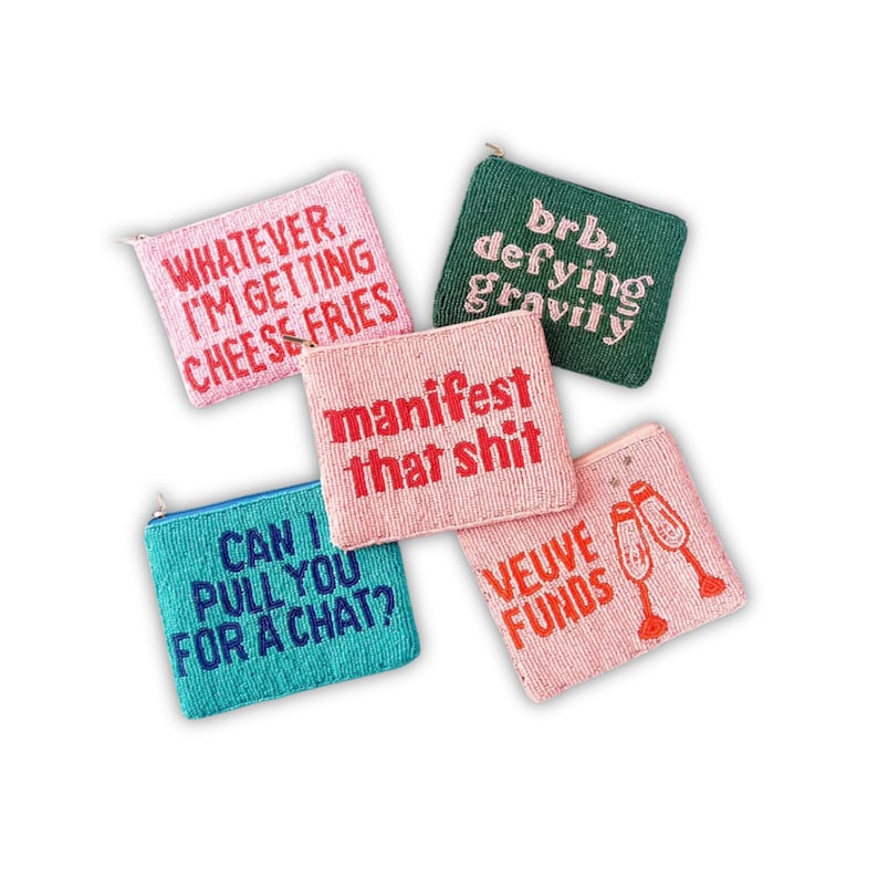 May include: Five beaded pouches in pink, green, and teal. Each pouch has a different phrase embroidered on it: "Whatever, I'm getting cheese fries", "brb, defying gravity", "manifest that shit", "Can I pull you for a chat?", and "Veuve Funds".