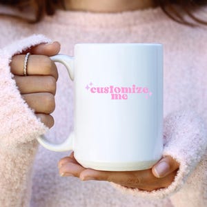 May include: White ceramic mug with a pink design that says "customize me" with pink stars on either side of the text.