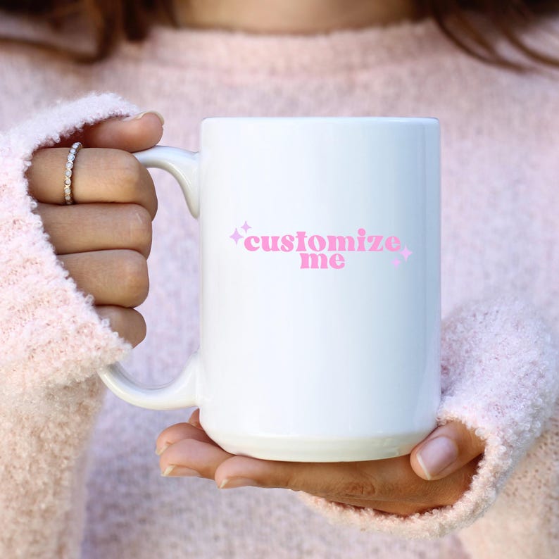 May include: White ceramic mug with a pink design that says "customize me" with pink stars on either side of the text.