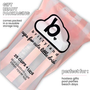 Op de afbeelding: Een herbruikbare opbergtas met roze en witte verticale strepen met 25 bekers en deksels. De tas bevat de tekst: GIFT READY PACKAGING, brittyland cups for cute little drinks, 25 CUPS + LIDS, 16oz u bottom cups, 95mm sipper lids.