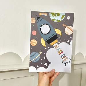 Pode incluir: Um foguete azul e amarelo com um c&iacute;rculo branco no meio, voando pelo espa&ccedil;o com planetas e estrelas. O texto "BLAST OFF" est&aacute; escrito em letras coloridas na lateral do foguete.