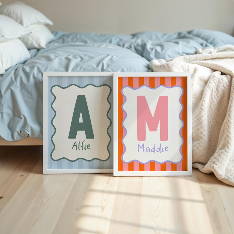 Puede incluir: Dos impresiones enmarcadas con rayas coloridas y bordes ondulados. La primera impresi&oacute;n presenta una gran "A" verde con el nombre "Alfie" debajo. La segunda impresi&oacute;n presenta una gran "M" rosa con el nombre "Maddie" debajo.