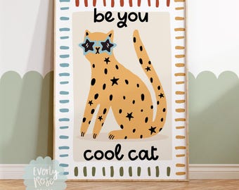 May include: A framed art print featuring a cartoon cat with star-shaped sunglasses. The cat is orange with black spots and stars. The text reads "be you cool cat" in black. The print has a cream background and a decorative border.