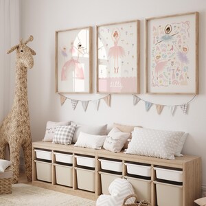 May include: A light wood bench with storage bins and a light gray cushion. Three framed prints with illustrations of ballerinas in pink dresses and floral designs hang on the wall above the bench. A light brown giraffe figurine stands to the left of the bench.