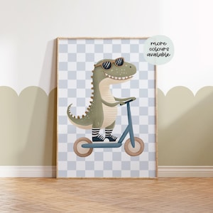 Op de afbeelding: Een groene dinosaurus met een zonnebril en zwart-wit gestreepte sokken rijdt op een blauwe scooter op een lichtblauwe en witte geruite achtergrond. De tekst "meer kleuren beschikbaar" staat in een cirkel aan de rechterkant van de afbeelding.