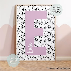 May include: A pink letter E with the name "Evie" written inside, on a white background with black polka dots. The print is framed and has a note that says "more colours available".