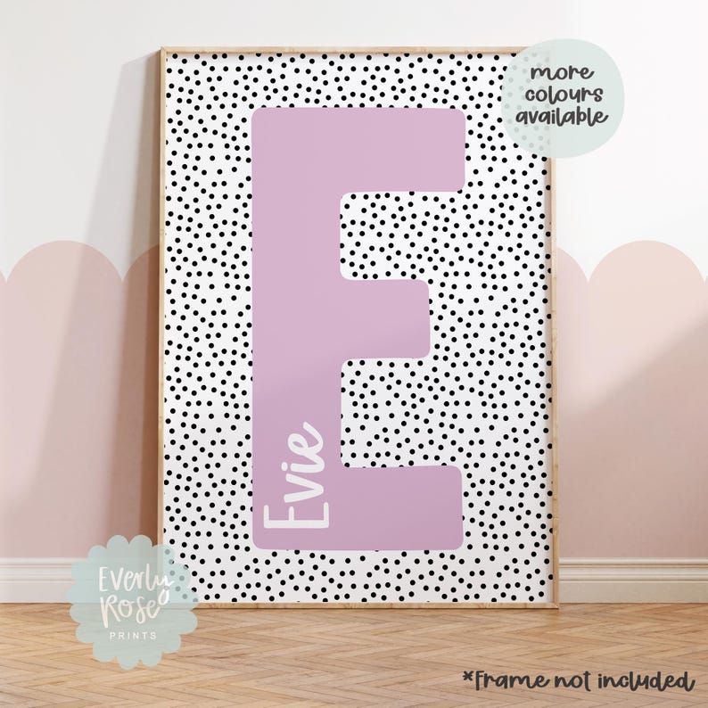 May include: A pink letter E with the name "Evie" written inside, on a white background with black polka dots. The print is framed and has a note that says "more colours available".