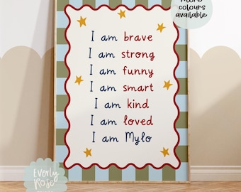 May include: A framed print with a white background and red scalloped border. The print features the phrases "I am brave," "I am strong," and others in a playful font, with yellow star accents. The words "more colours available" are also visible.