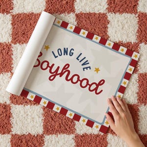 May include: A rolled-up poster with the words "LONG LIVE Boyhood" in red and blue lettering, surrounded by a red and white border with yellow stars. The poster is partially unrolled, revealing the text on a cream background.