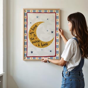 K&ouml;nnte beinhalten: Ein gerahmter Druck mit einem gelben Halbmond und Sternen, mit dem Text "love you to the moon & back". Der Druck hat einen rot-blauen Rand mit einem hellen Holzrahmen. Der Hintergrund ist wei&szlig;.