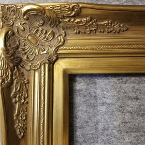 May include: A gold ornate picture frame with a detailed, carved design. The frame has a slightly rounded edge and a smooth, polished finish.