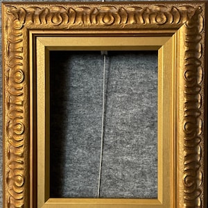 May include: A gold picture frame with an ornate design. The frame is made of wood and has a smooth, polished finish.