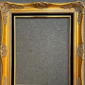 May include: Ornate gold picture frame with a black inner border. The frame has detailed scrollwork and decorative elements. The frame is rectangular and has a vintage or antique aesthetic.