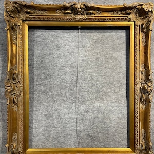 May include: A large, ornate, gold-colored picture frame with a carved design. The frame is made of wood and has a distressed finish.
