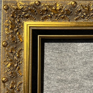 May include: A gold picture frame with a black mat and ornate, embossed details. The frame has a raised, textured design with a floral motif.