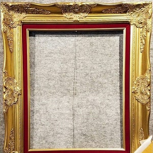 May include: A gold picture frame with ornate details and a red velvet mat. The frame is empty and ready for a picture.