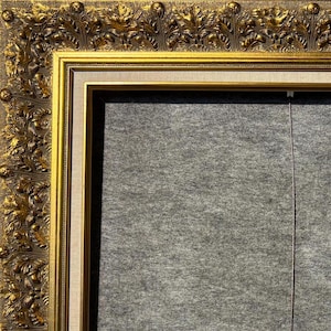 May include: A gold picture frame with an ornate design. The frame has a white mat and a gray backing.
