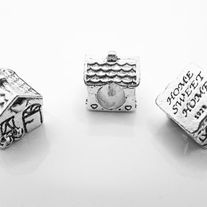 May include: Three silver charm beads in the shape of a house. The first bead is a detailed house with a door and windows. The second bead is a simple house with a roof. The third bead is a house with the text "Home Sweet Home 1979 NL" engraved on it.