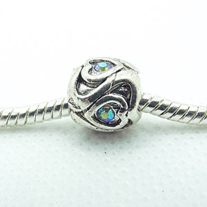 May include: Silver charm bead with two iridescent blue gemstones set in a heart design.