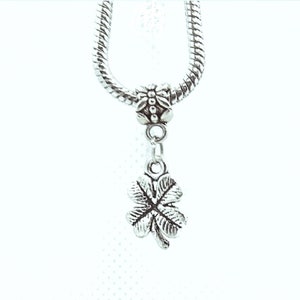 May include: Silver charm necklace with a four-leaf clover pendant. The charm is attached to a silver chain with a silver bead.