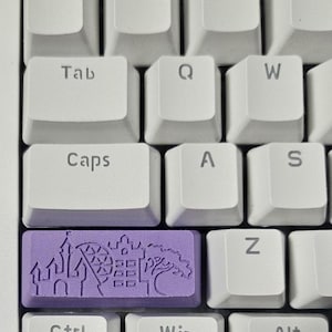 Puede incluir: Una tecla de teclado púrpura con un diseño de un castillo, una noria y un árbol. La tecla está etiquetada con la palabra "Ctrl".