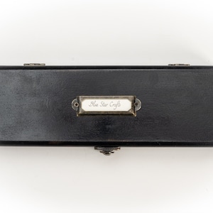 Puede incluir: Una caja rectangular negra con una etiqueta de latón que dice "Blue Star Crafts".