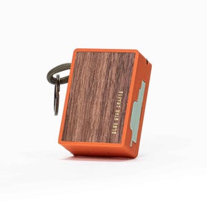 Może przedstawiać: Pomarańczowe pudełko z drewnianym panelem przednim i pionowo wydrukowanym tekstem "BLUE STAR CRAFTS". Zielony pasek i metalowe zapięcie są przymocowane u góry. Bok pudełka ma jasnozielony wzór.