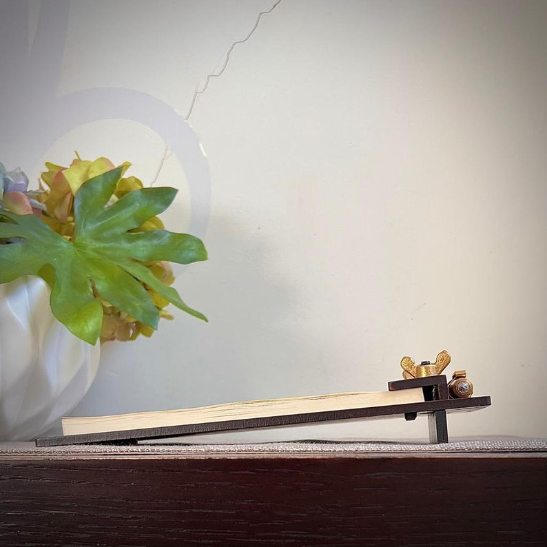 May include: A wooden guitar capo with a brass adjustment knob. The capo is positioned on a wooden surface.