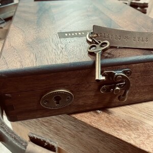 Puede incluir: Una caja de madera con una cerradura de lat&oacute;n y un pestillo. La caja tiene una correa de cuero y una etiqueta de cuero que dice "STAR CRAFTS".