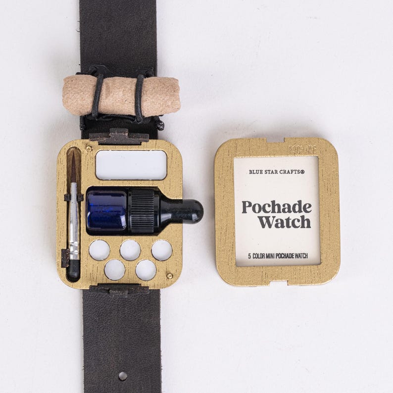 May include: A gold-colored Pochade Watch, a miniature watercolor palette, with a black leather strap. The watch case holds a small brush, a blue paint bottle, and a white mixing area. The watch is open, revealing the 5-color mini palette.