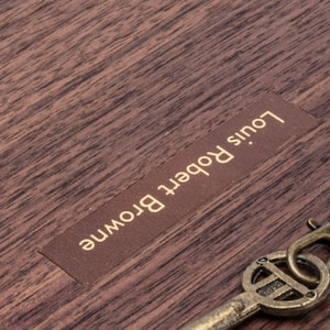 Puede incluir: Una caja de madera con una etiqueta de cuero marr&oacute;n que dice "Louis Robert Browne".