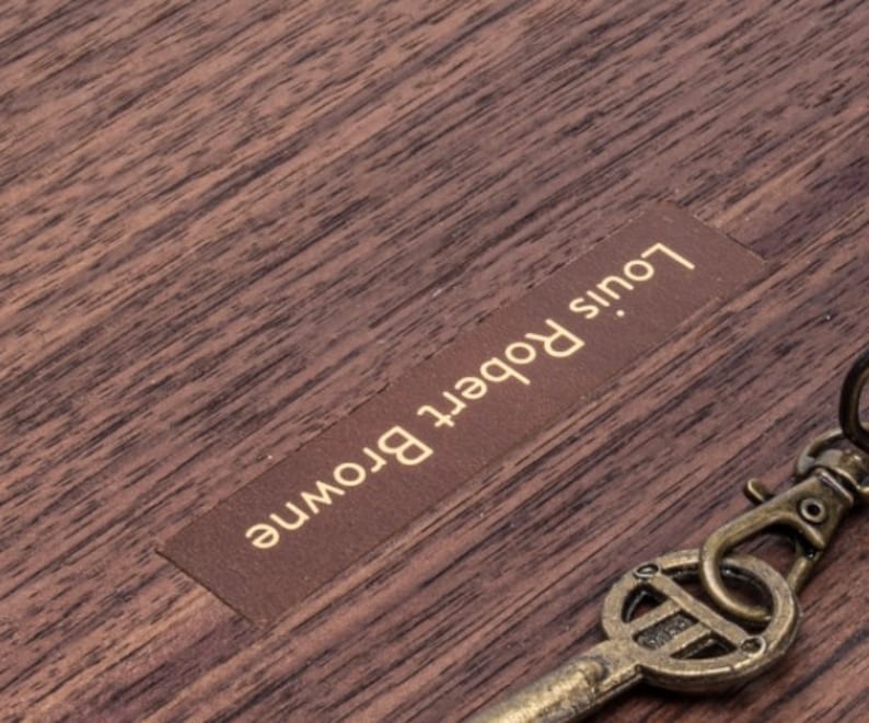 Puede incluir: Una caja de madera con una etiqueta de cuero marr&oacute;n que dice "Louis Robert Browne".