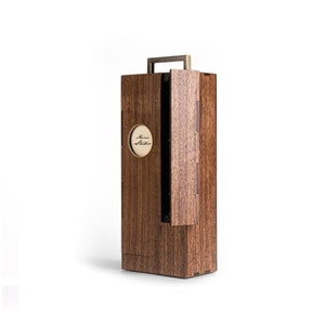 Puede incluir: Una caja de madera marrón oscuro con asa y puerta abatible. La caja tiene un asa de color latón. Un pequeño emblema redondo de color dorado con las palabras "Mini Studio" está en la parte delantera.