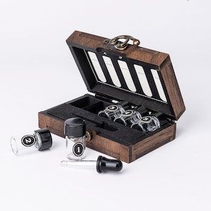 May include: A wooden box with a hinged lid, containing five small glass bottles with droppers. The bottles are labeled with numbers 1 through 5. The box is open and the bottles are visible. There is a dropper on the table next to the box.