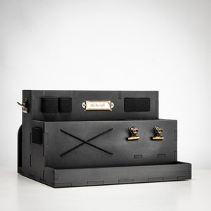 Puede incluir: Organizador de escritorio negro con una etiqueta que dice "The Star Craft". Tiene dos clips y un pequeño estante en la parte inferior.