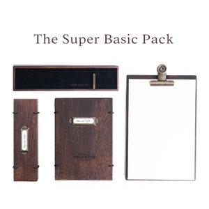 Puede incluir: El paquete Super Basic incluye una bandeja de madera, un cuaderno de madera, una tabla de madera y un portaplumas de madera. Todos los artículos son de color marrón y tienen un aspecto rústico. El texto "Super Basic Tray" es visible en la bandeja. El texto "Field Notes" es visible en el cuaderno. El texto "Blue Star Coffee" es visible en una etiqueta en el cuaderno y el portaplumas.