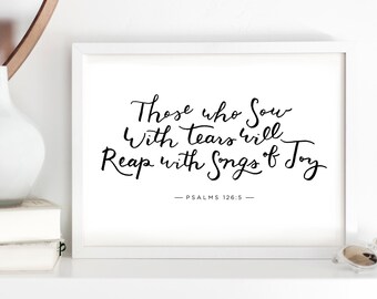 May include: A white framed print with black calligraphy that reads "Those who sow with tears will reap with songs of joy" and "Psalms 126:5".