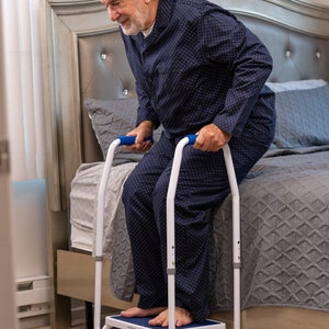 May include: A white metal step stool with blue accents and two handrails. The step stool has a non-slip surface and is designed to help people get in and out of bed.