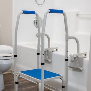 May include: A white and blue bathroom safety step stool with two grab bars. The step stool has a blue non-slip surface and the grab bars have blue handles. The step stool is in a bathroom with a white bathtub and a white toilet.