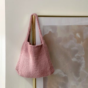 Puede incluir: Una bolsa de mano de punto de color rosa colgada de un marco dorado.