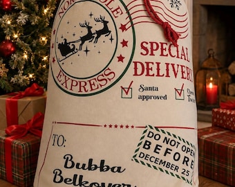 May include: A cream-colored canvas gift sack with a red drawstring closure. The front features a North Pole Express graphic with a reindeer sleigh, red and green text, and a stamp reading Do Not Open Before December 25. It is addressed to Bubba Belkover from Santa Claus.