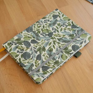 May include: A notebook with a green and white floral pattern and a grey ribbon closure. The notebook has a yellow bookmark.