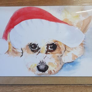 May include: Watercolour painting of a dog wearing a red and white Santa hat. The dog is looking at the viewer with a sweet expression.