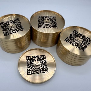 May include: A stack of ten gold-colored coasters with a black QR code and the word "MENU" printed on each coaster.