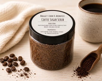 May include: A clear plastic jar filled with brown coffee sugar scrub, topped with a black lid featuring a white label that reads Maggie's Farm & Aromatics Coffee Sugar Scrub, including directions and ingredients, surrounded by coffee beans.